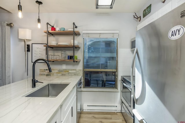 kitchen with appliances with stainless steel finishes, light stone counters, a baseboard heating unit, sink, and white cabinets