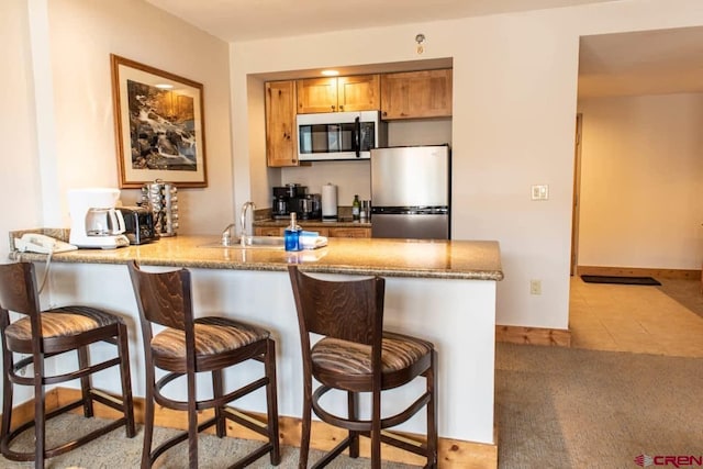 kitchen with kitchen peninsula, light carpet, a breakfast bar, and stainless steel appliances