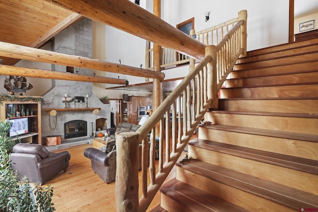 staircase with wood-type flooring, high vaulted ceiling, and a fireplace