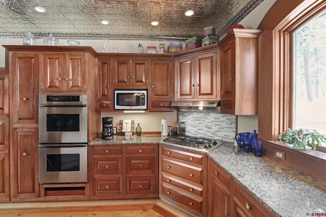 kitchen with stainless steel appliances, light stone counters, light hardwood / wood-style flooring, a wealth of natural light, and backsplash