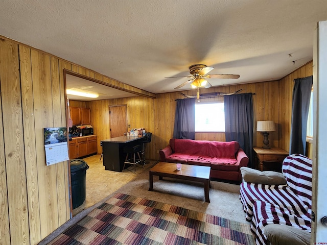 carpeted living room featuring wood walls, ceiling fan, and a textured ceiling