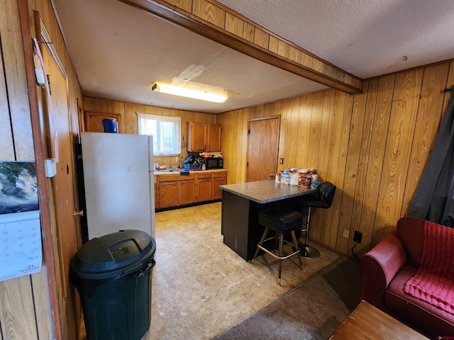 kitchen with a textured ceiling, wooden walls, a kitchen bar, a kitchen island, and white refrigerator