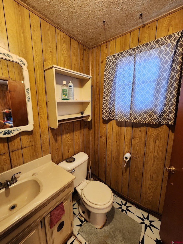 bathroom with wooden walls, a textured ceiling, tile patterned flooring, toilet, and vanity