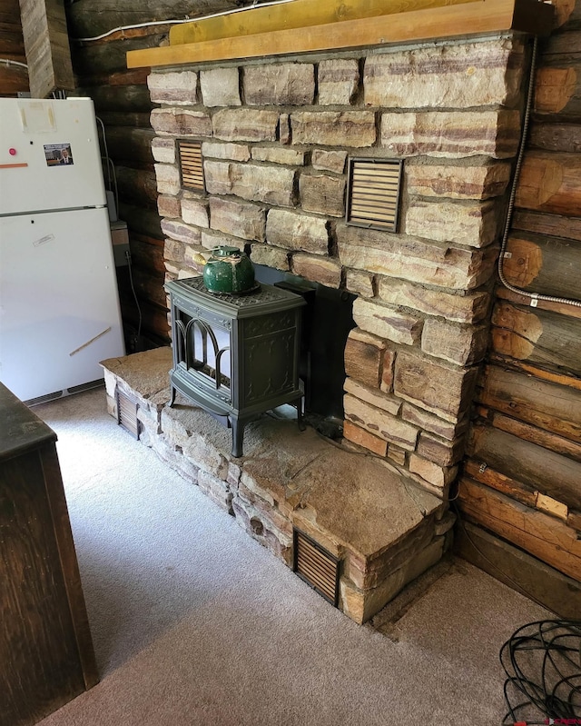 room details featuring carpet floors, log walls, white fridge, and a wood stove