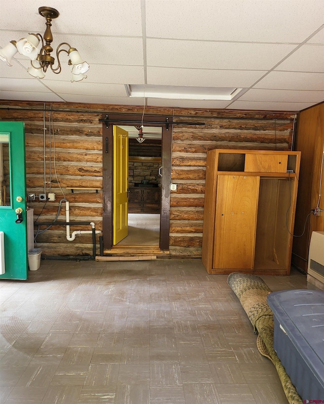 interior space featuring a notable chandelier, a paneled ceiling, log walls, and a barn door