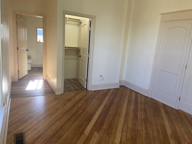 unfurnished bedroom with a walk in closet, a closet, and dark hardwood / wood-style floors