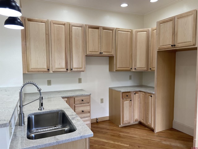 kitchen with light stone countertops, hanging light fixtures, light brown cabinetry, light hardwood / wood-style floors, and sink