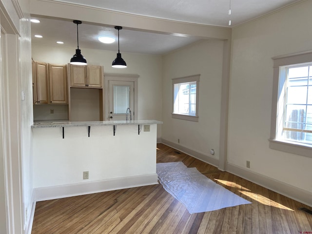 kitchen with sink, a breakfast bar area, light brown cabinetry, light stone countertops, and dark wood-type flooring