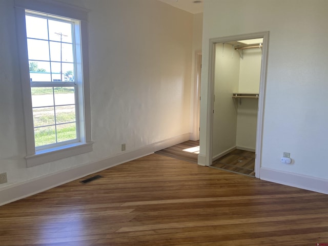 unfurnished bedroom featuring dark wood-type flooring, a walk in closet, and a closet