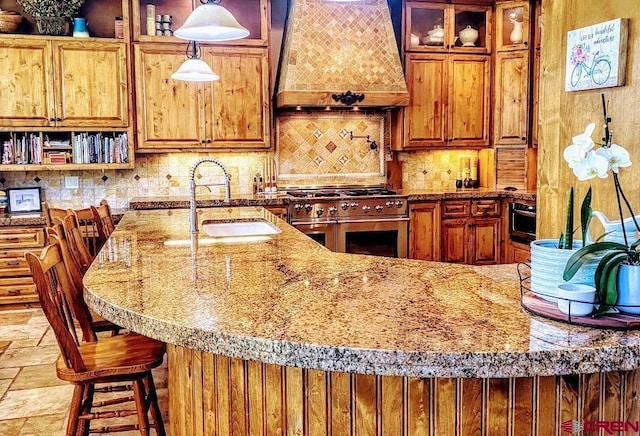 kitchen featuring sink, decorative backsplash, custom range hood, pendant lighting, and range with two ovens