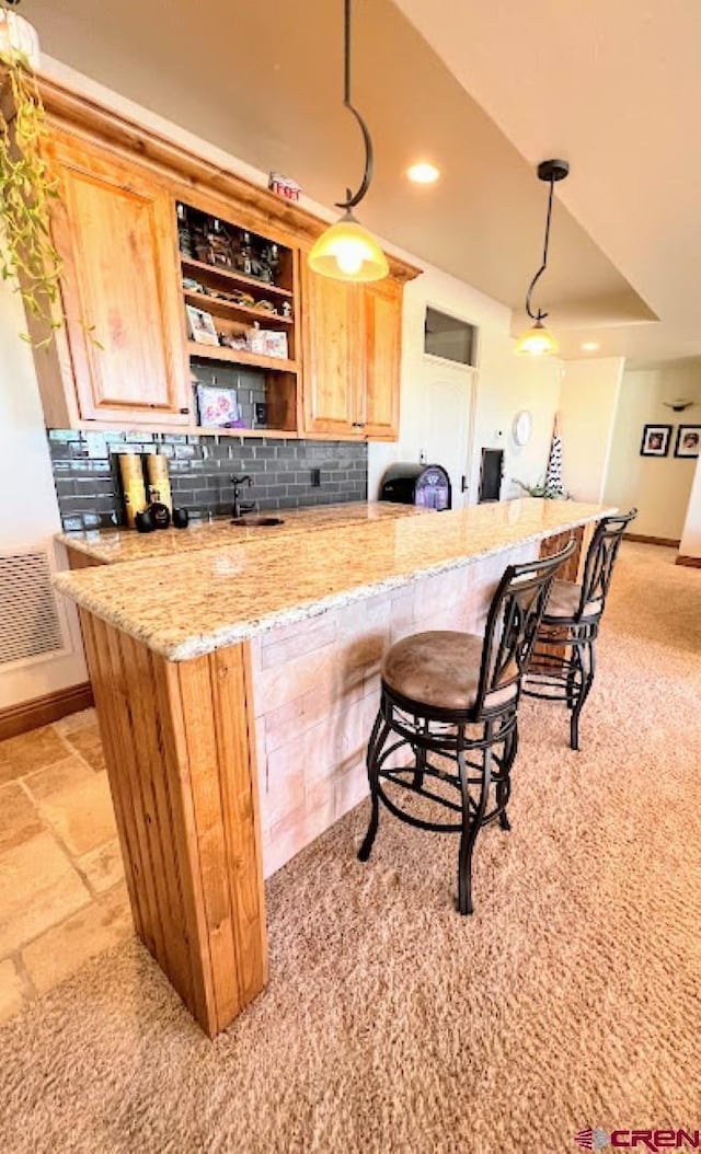 bar with sink, hanging light fixtures, backsplash, light stone counters, and light brown cabinetry