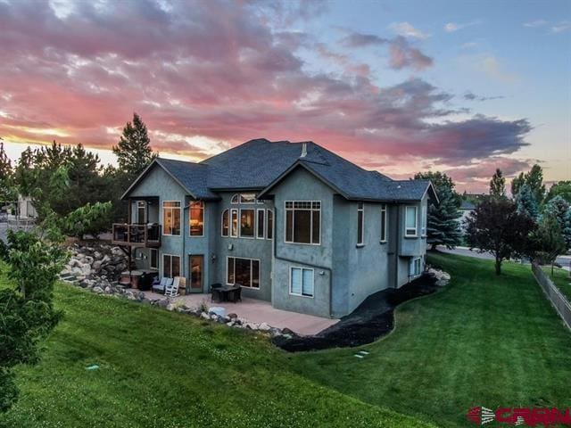 back house at dusk featuring a balcony, a yard, and a patio