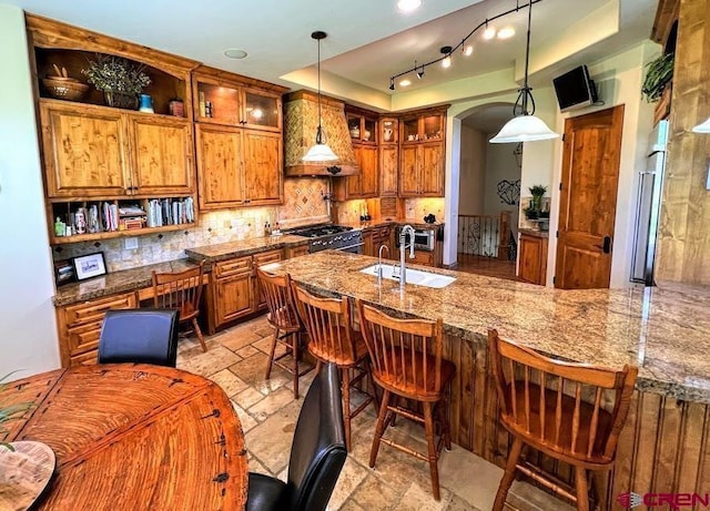 kitchen with gas stove, sink, a tray ceiling, kitchen peninsula, and custom range hood