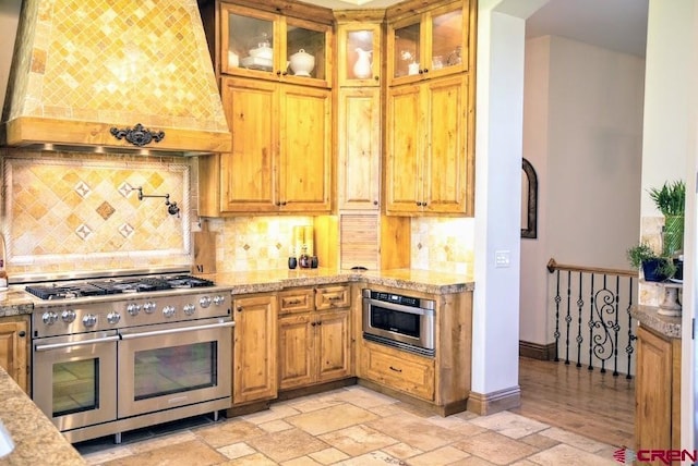 kitchen featuring light stone countertops, decorative backsplash, custom exhaust hood, and stainless steel appliances