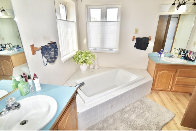 bathroom with hardwood / wood-style flooring, a relaxing tiled tub, and vanity