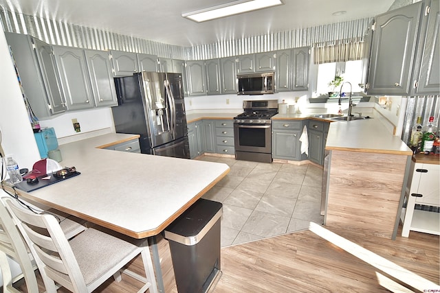 kitchen with stainless steel appliances, sink, light tile patterned floors, kitchen peninsula, and gray cabinetry