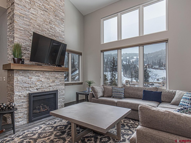 living room with a towering ceiling, wood-type flooring, and a stone fireplace