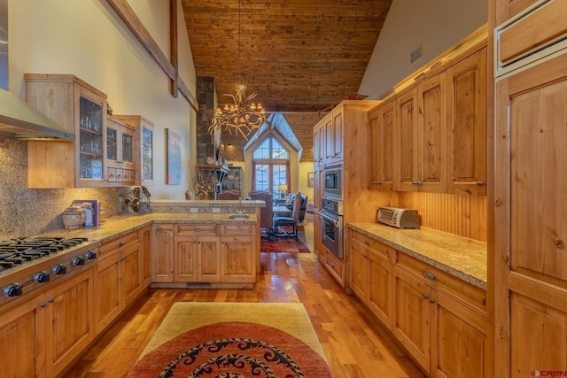 kitchen featuring wall chimney exhaust hood, light hardwood / wood-style flooring, decorative backsplash, a notable chandelier, and appliances with stainless steel finishes