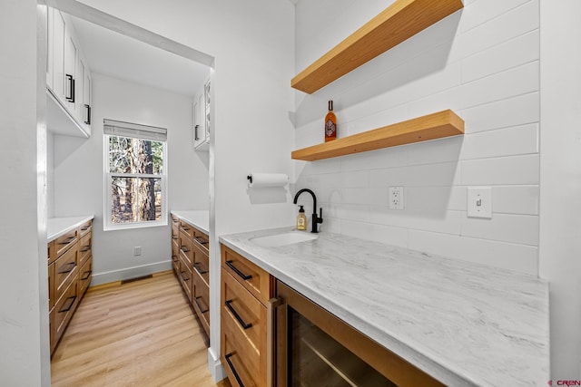 kitchen with tasteful backsplash, light stone countertops, sink, and light hardwood / wood-style floors