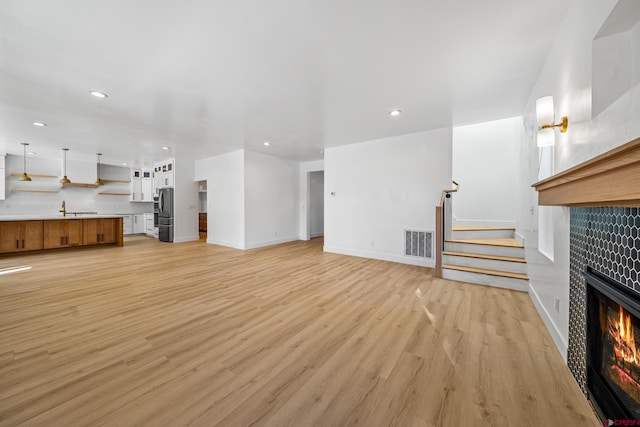 unfurnished living room with light wood-type flooring, a tile fireplace, and sink