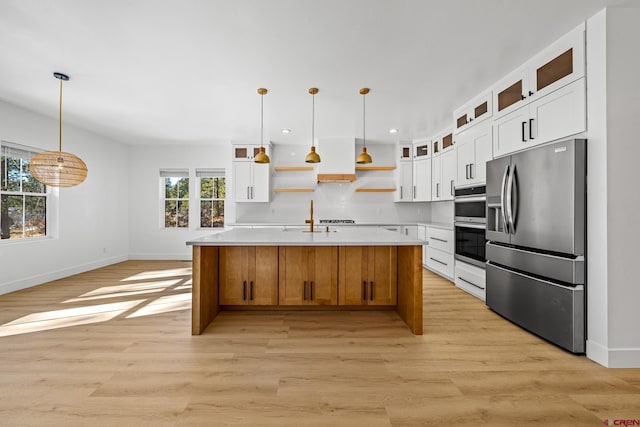 kitchen with stainless steel appliances, white cabinets, a center island with sink, and hanging light fixtures