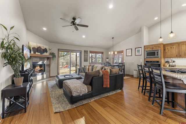 living room with ceiling fan with notable chandelier, vaulted ceiling, a premium fireplace, and light wood-type flooring