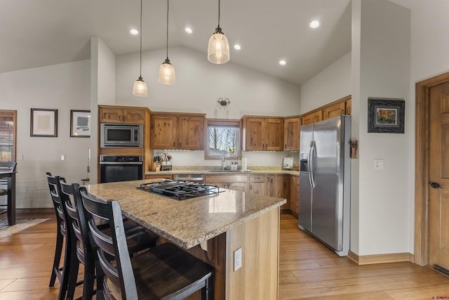 kitchen featuring stainless steel appliances, a center island, light stone countertops, a breakfast bar, and sink