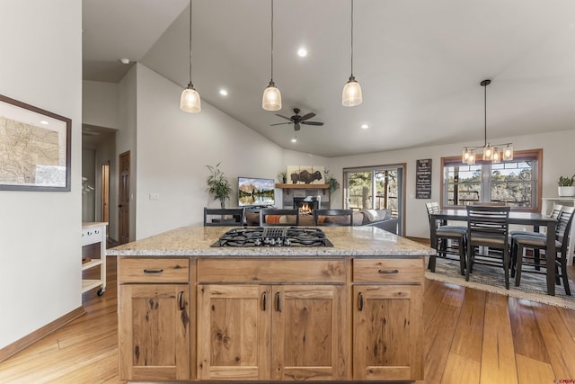 kitchen with decorative light fixtures, a fireplace, stainless steel gas cooktop, light stone countertops, and ceiling fan with notable chandelier