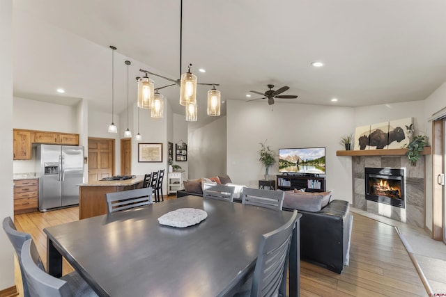 dining room with ceiling fan, light hardwood / wood-style flooring, high vaulted ceiling, and a fireplace