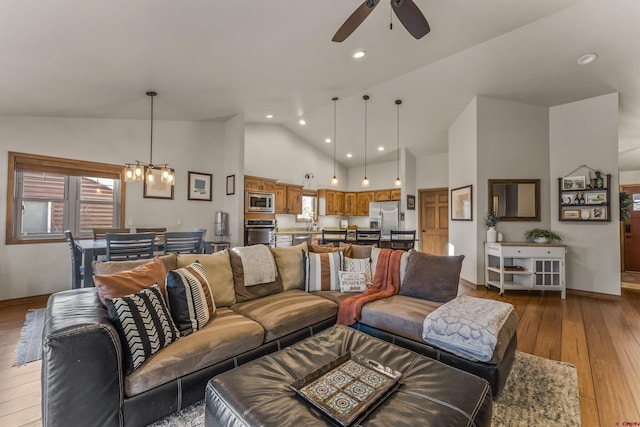 living room with high vaulted ceiling, a healthy amount of sunlight, light wood-type flooring, and ceiling fan with notable chandelier