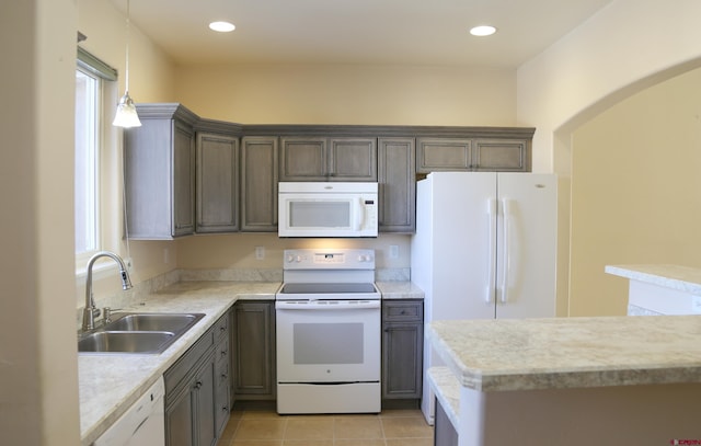 kitchen with sink, white appliances, light tile patterned flooring, hanging light fixtures, and a healthy amount of sunlight