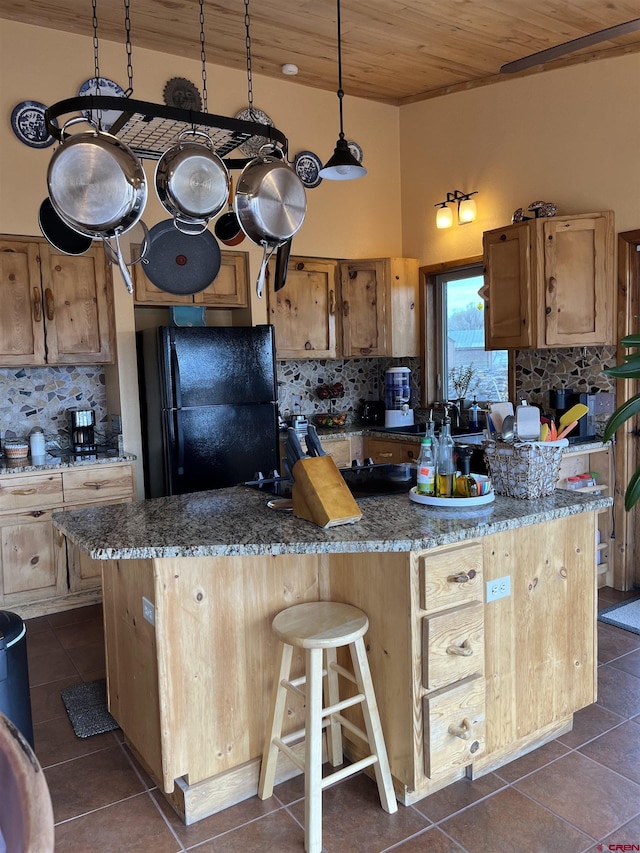 kitchen with a center island, tasteful backsplash, stone countertops, black fridge, and wooden ceiling