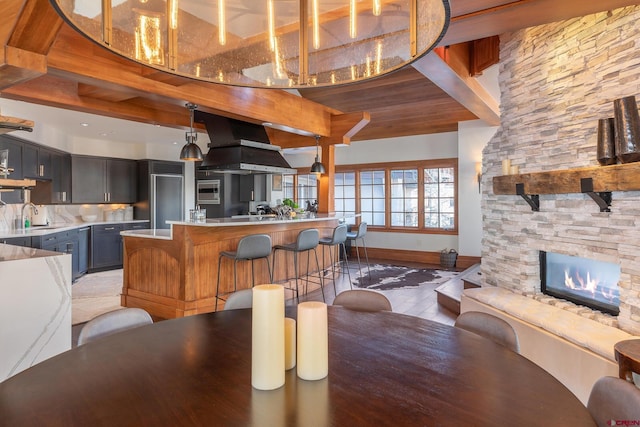 dining space with beam ceiling, light hardwood / wood-style floors, a stone fireplace, and sink