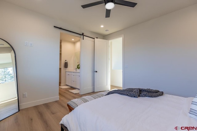 bedroom with ceiling fan, a barn door, ensuite bathroom, and light hardwood / wood-style flooring