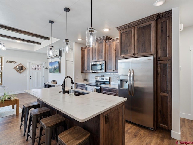 kitchen featuring pendant lighting, beam ceiling, sink, appliances with stainless steel finishes, and an island with sink