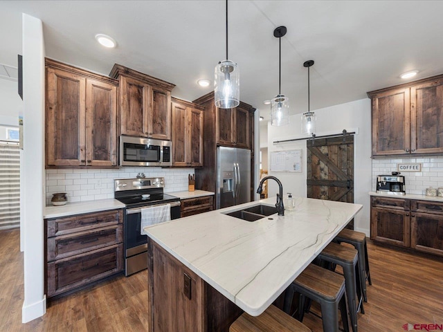 kitchen featuring a barn door, a kitchen island with sink, and appliances with stainless steel finishes