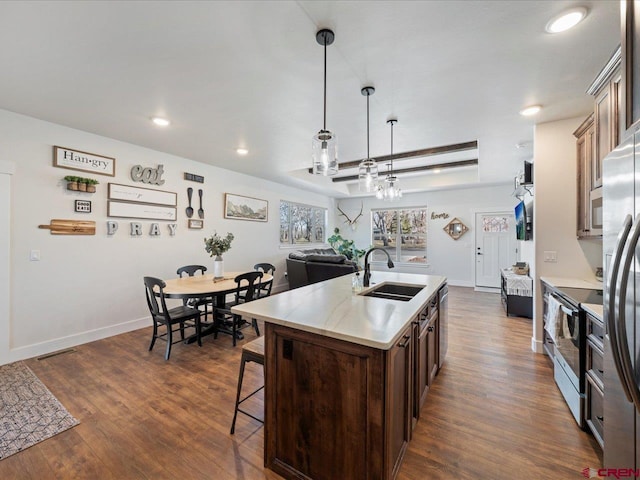 kitchen with pendant lighting, dark brown cabinetry, an island with sink, sink, and a tray ceiling