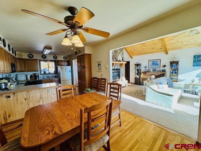 dining room with light wood-type flooring, ceiling fan, a fireplace, and beamed ceiling