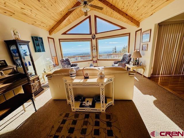 interior space with ceiling fan, lofted ceiling with beams, wood ceiling, and dark carpet