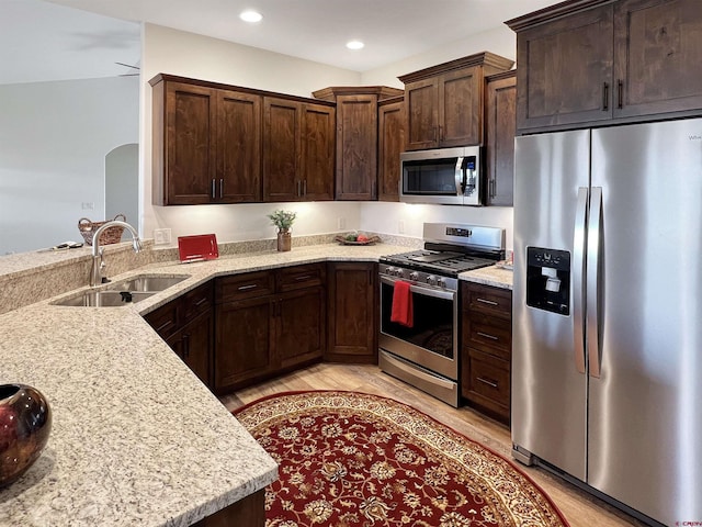 kitchen with kitchen peninsula, sink, light hardwood / wood-style flooring, stainless steel appliances, and light stone counters