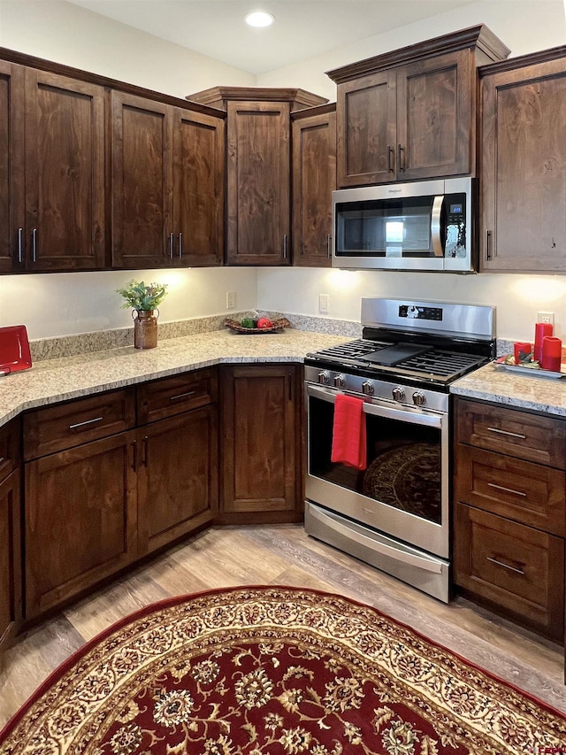 kitchen with light stone counters, dark brown cabinets, light hardwood / wood-style flooring, and stainless steel appliances