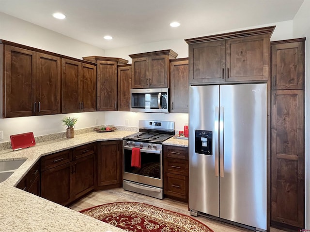 kitchen featuring light stone countertops, sink, stainless steel appliances, and dark brown cabinets