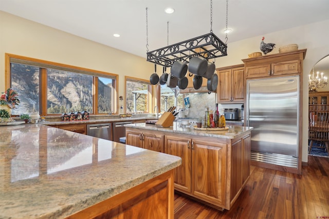 kitchen featuring appliances with stainless steel finishes, dark wood-type flooring, light stone countertops, pendant lighting, and a center island