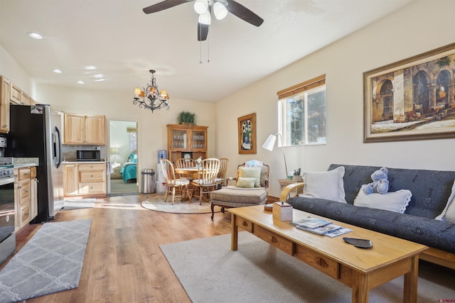 living room featuring ceiling fan with notable chandelier and light hardwood / wood-style flooring