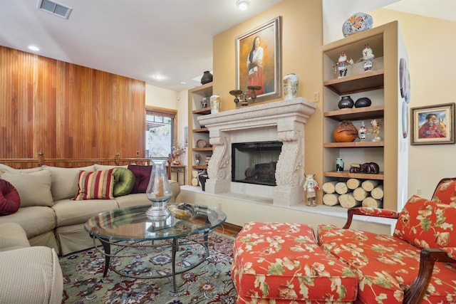 living room with a high end fireplace, built in features, and wood walls