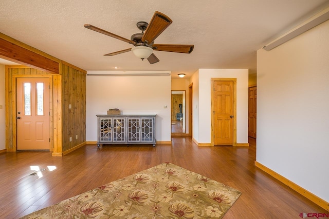 unfurnished living room featuring ceiling fan, a textured ceiling, dark hardwood / wood-style floors, and wood walls