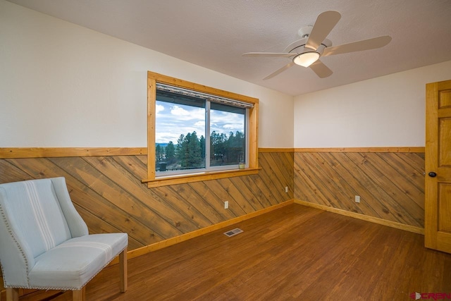 living area with ceiling fan, hardwood / wood-style flooring, and wood walls