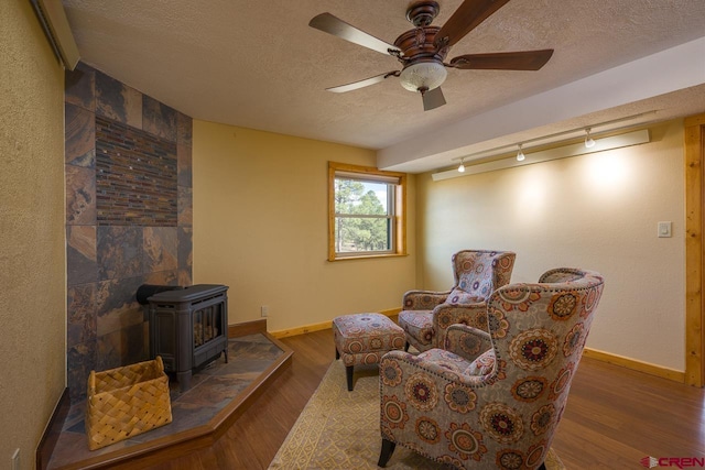 sitting room with a textured ceiling, rail lighting, a wood stove, and dark hardwood / wood-style floors