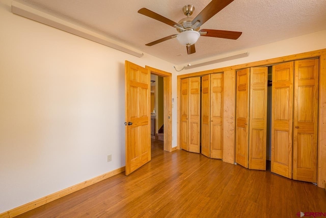 unfurnished bedroom featuring ceiling fan, two closets, a textured ceiling, and wood-type flooring