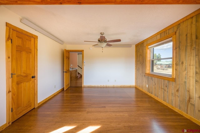 spare room featuring ceiling fan, dark hardwood / wood-style flooring, and wood walls